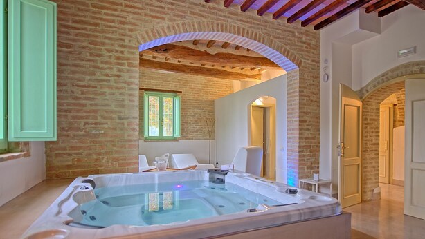 Un espace de détente avec un jacuzzi, deux chaises blanches et une fenêtre avec des volets verts.