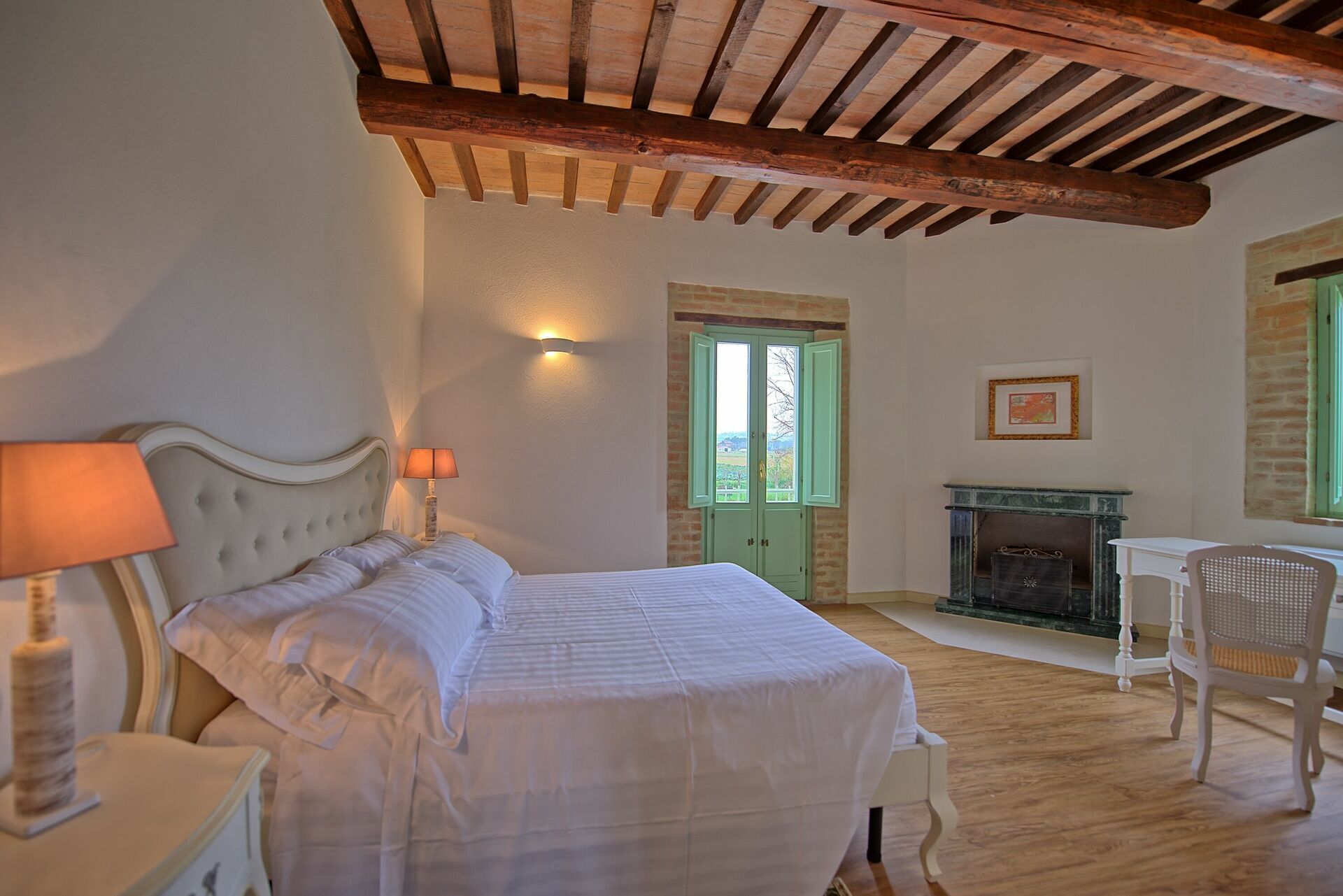 Un dormitorio con cama, mesita de noche, lámpara, puerta verde, chimenea y una silla.