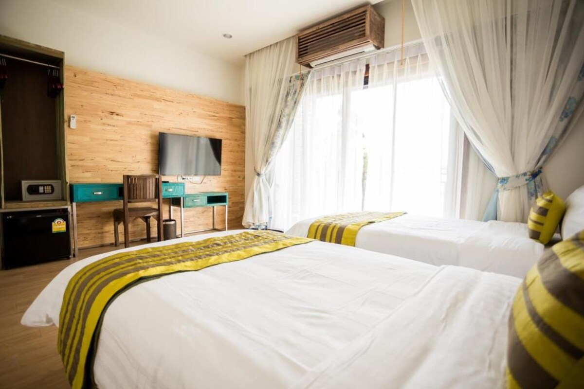 Une chambre d’hôtel avec deux lits, un bureau, une télévision et une fenêtre avec des rideaux.