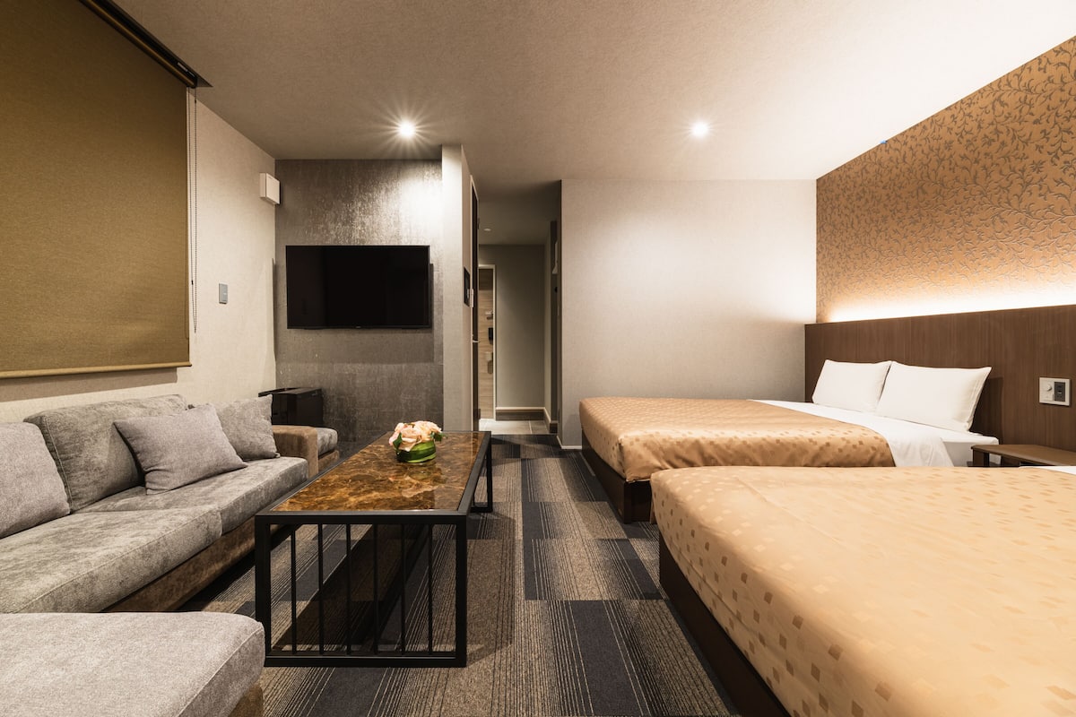 A hotel room with a sofa, a coffee table, two single beds, and a TV mounted on the wall.