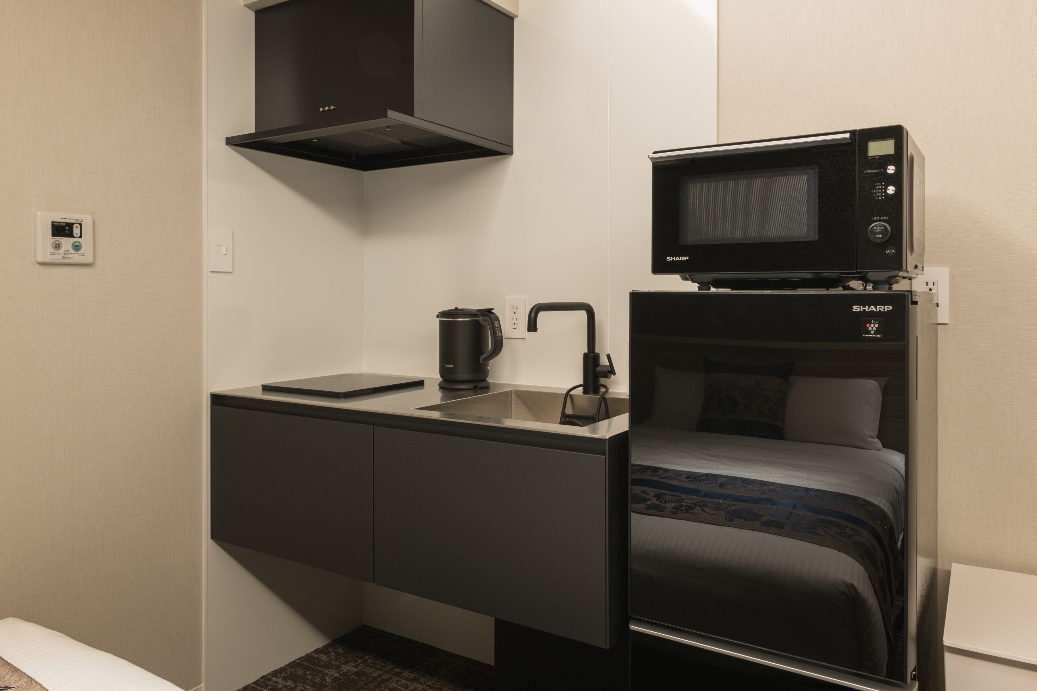 Habitación de hotel compacta con cama, una kitchenette pequeña, microondas y termostato digital.