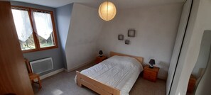 Ein Schlafzimmer mit Bett, Nachttischen, einer Lampe, einem Heizkörper und einem Fenster mit Vorhängen.