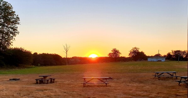 Ein Picknickbereich mit Bänken und einem Picknicktisch, vor einer Sonnenuntergangslandschaft.
