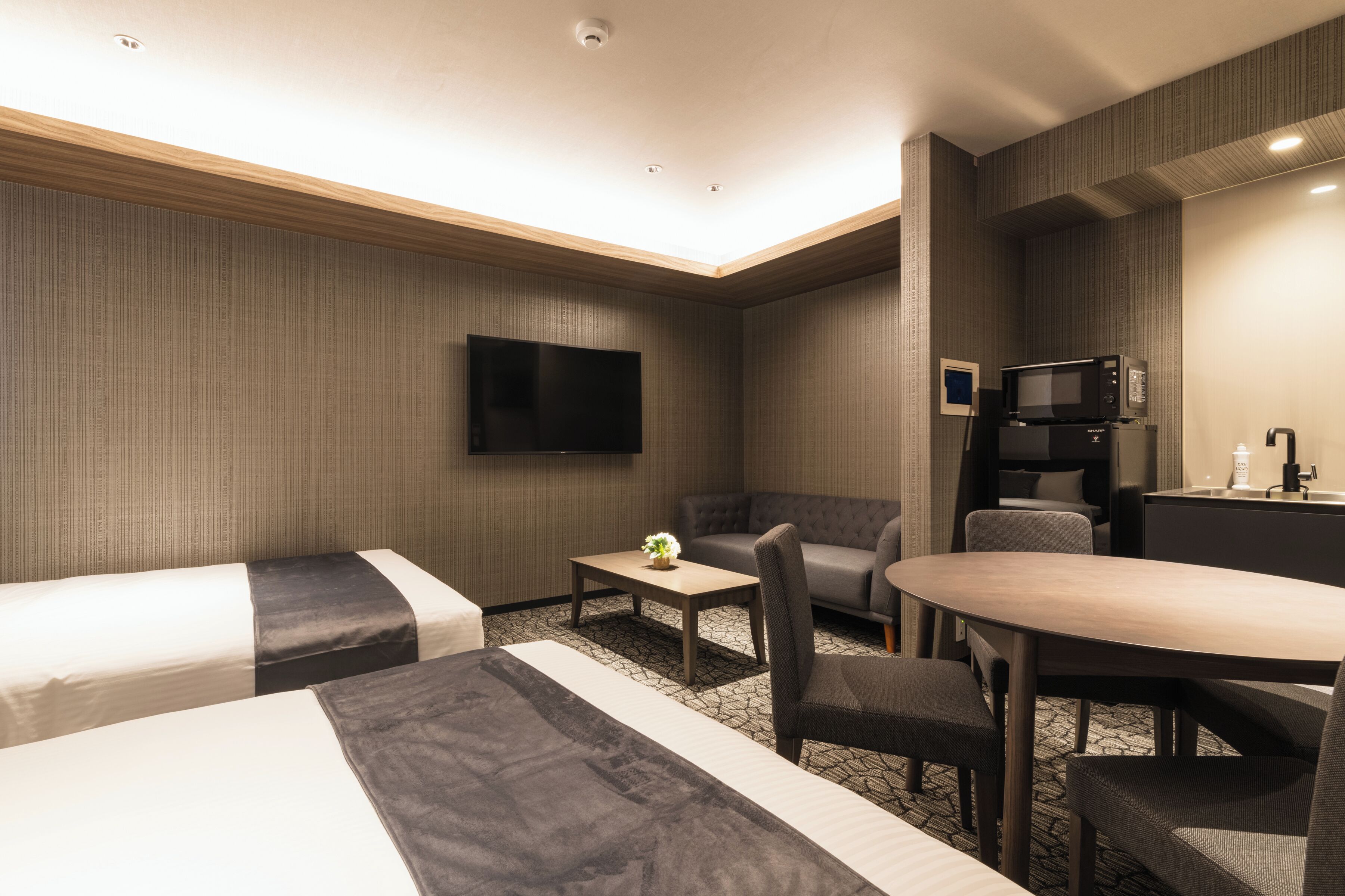 Habitación de hotel con dos camas individuales, un sofá, una mesa de comedor, un televisor y un microondas.