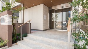 En modern entré till en byggnad med en trappa som leder till en glasdörr, omgiven av grönska.