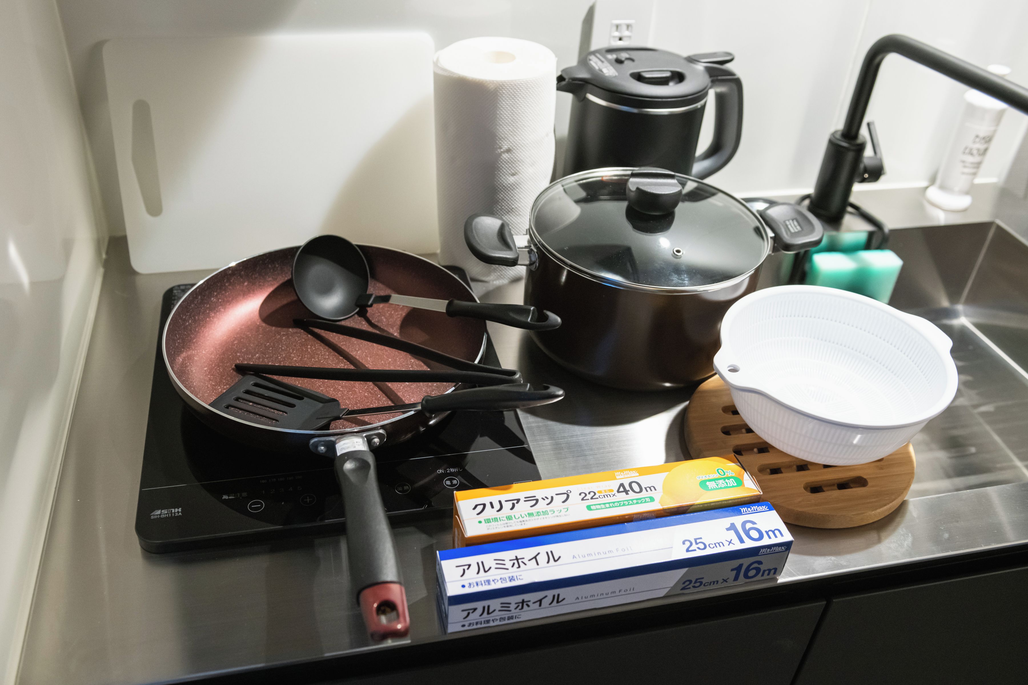 A kitchen with a stove, pots, a frying pan, a kettle, a rice cooker, and a box of aluminum foil.