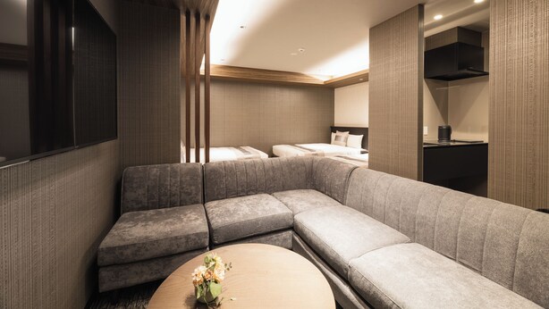Ett modernt hotellrum med en modulsoffa, ett runt soffbord och en säng med vita sängkläder.