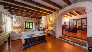 Une pièce chaleureuse avec un mur en pierre, des poutres apparentes, un canapé, une table avec des magazines et un escalier menant à un autre espace.