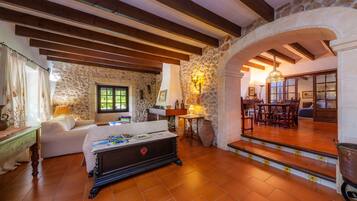 A cozy room with a stone wall, wooden beams, a sofa, a table with magazines, and a staircase leading to another area.