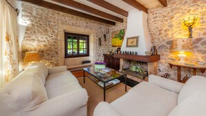 Un salon chaleureux avec des murs en pierre, des poutres apparentes, une cheminée et une table basse en verre.