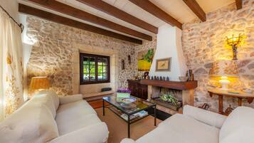 A cozy living room with stone walls, wooden beams, a fireplace, and a glass coffee table.