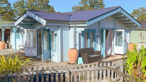 A two-story house with a wooden deck, a fenced yard, and a clear blue sky. - Secluded Countryside Lodge on 25 Acres | Private Deck & Views | Kent Escape (Biddenden)