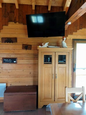 A wooden cabin interior with a mounted television, wooden cabinets, and a bench.