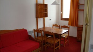 Ein Zimmer mit einem Holzesstisch, vier Stühlen, einem roten Sofa, einem Holzschrank und einem Fenster mit Vorhängen.