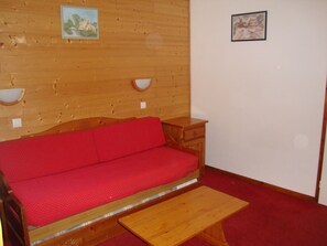 Ein Zimmer mit Holzboden, einem roten Sofa, einem Holztisch und zwei Wandlampen.