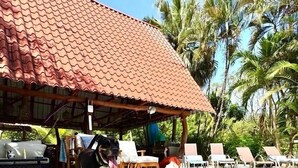 A covered outdoor area with a tiled roof, lounge chairs, and a pool.