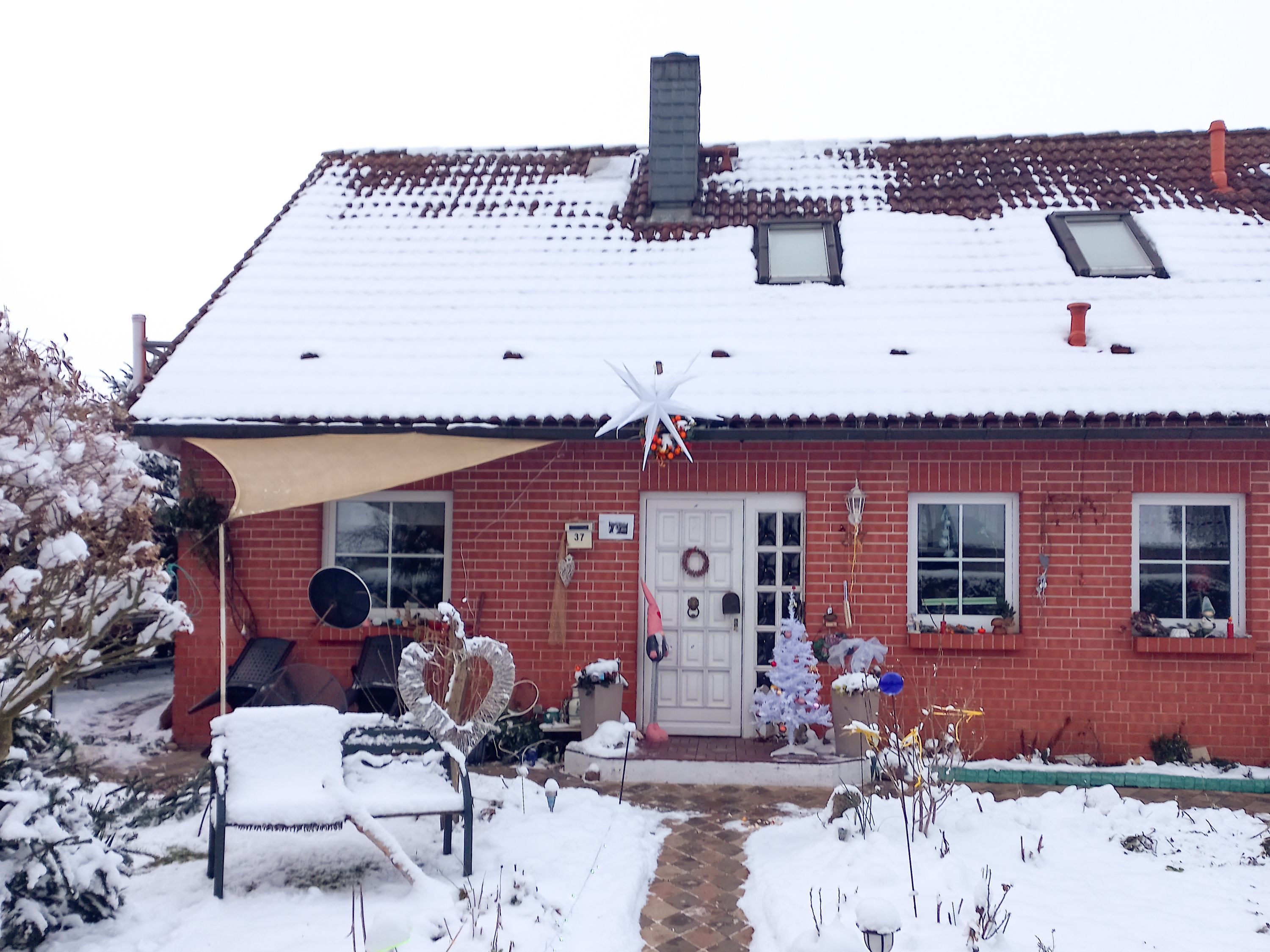 Ein rotes Backsteinhaus mit schneebedecktem Dach, einer weißen Tür und einem kleinen Fenster.