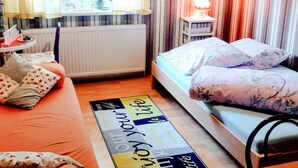 A bedroom with a bed, a side table, a lamp, a radiator, and a window with curtains.