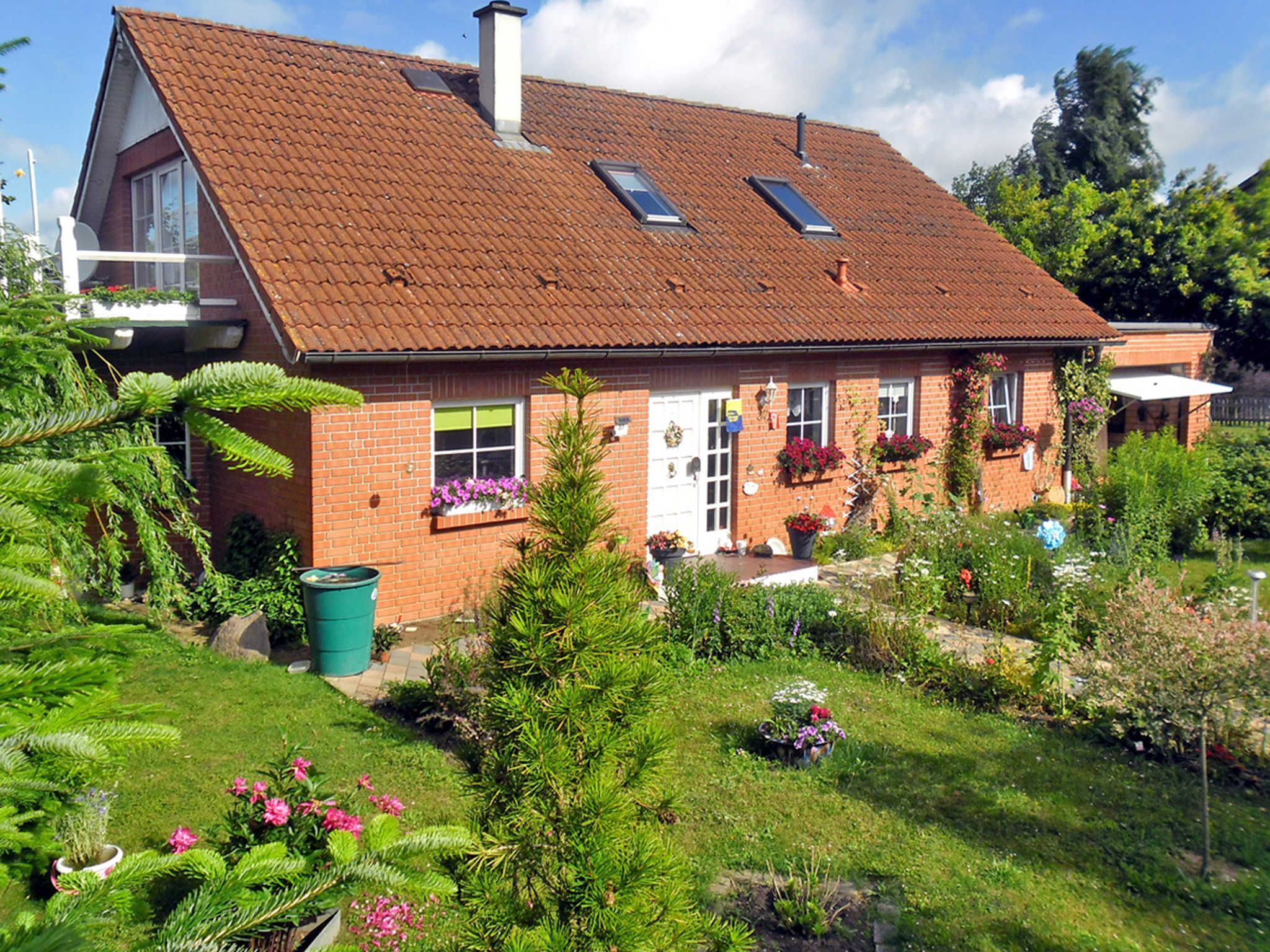 A two-story house with a sloped roof, a front porch, and a garden with various plants and flowers.