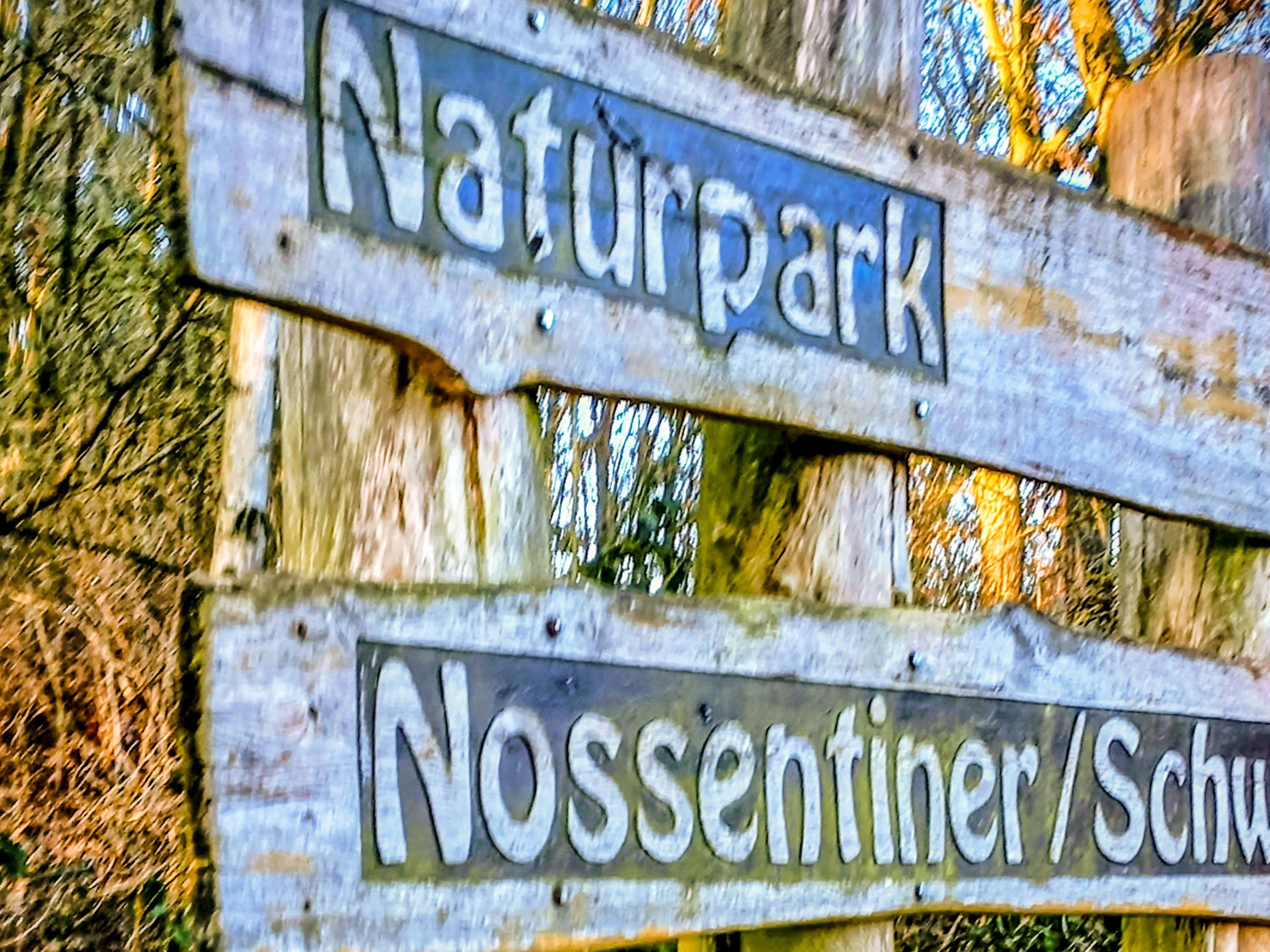 A wooden sign with the words 'Naturpark' and 'Nossentiner/Schu' indicating a park area.