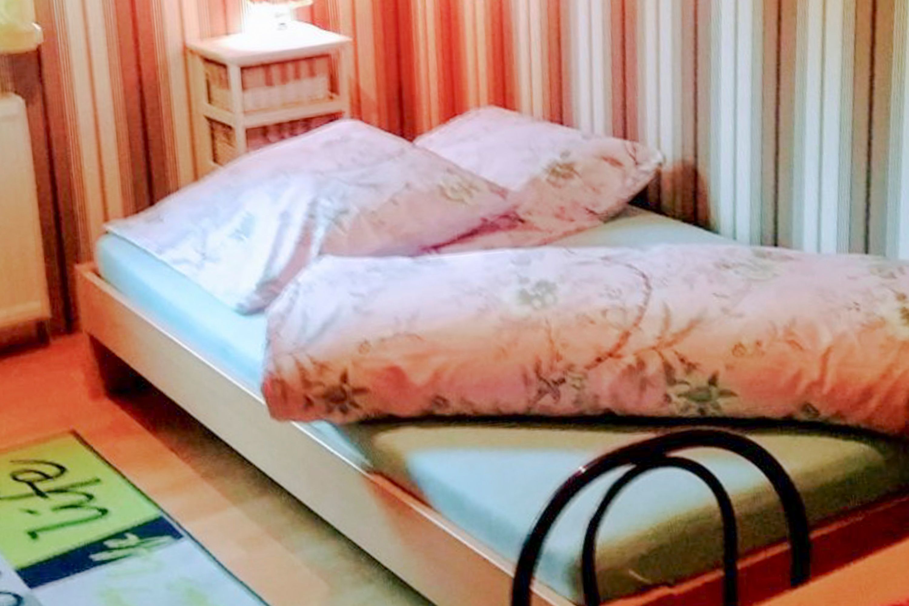 A bed with floral bedding, a bedside table, and a striped curtain backdrop.