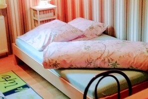 A bed with floral bedding, a bedside table, and a striped curtain backdrop. - Ferienzimmer Alt Sammit bei Krakow - Ferienzimmer (Krakow am See)