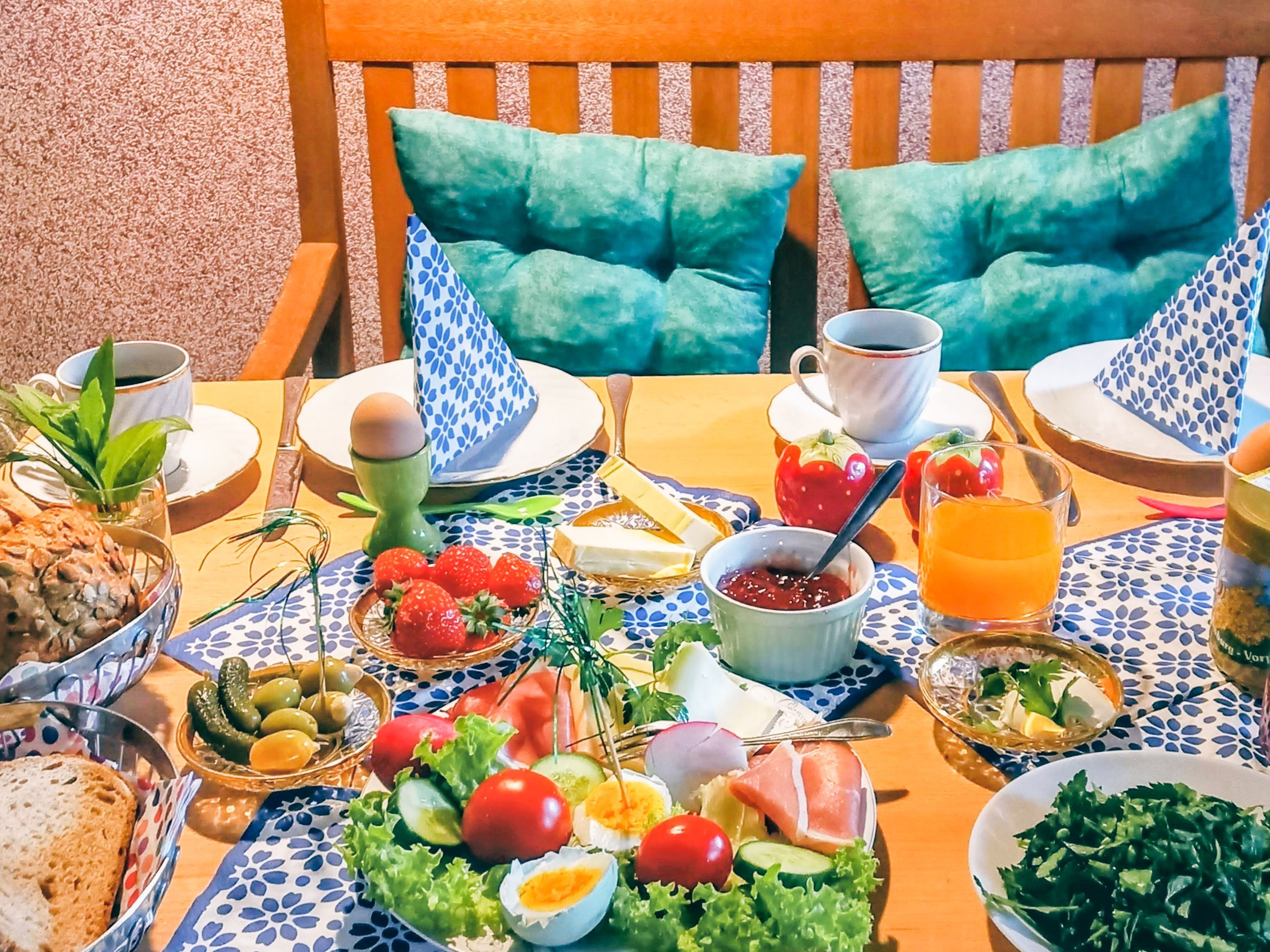 A table set with breakfast items including eggs, bread, and fruit, with a view of a wooden chair and a cushion.