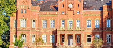 A large red brick building with a clock tower, multiple windows, and a red car parked in front.