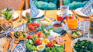 A table set with breakfast items including eggs, bread, and fruit, with a view of a wooden chair and a cushion.