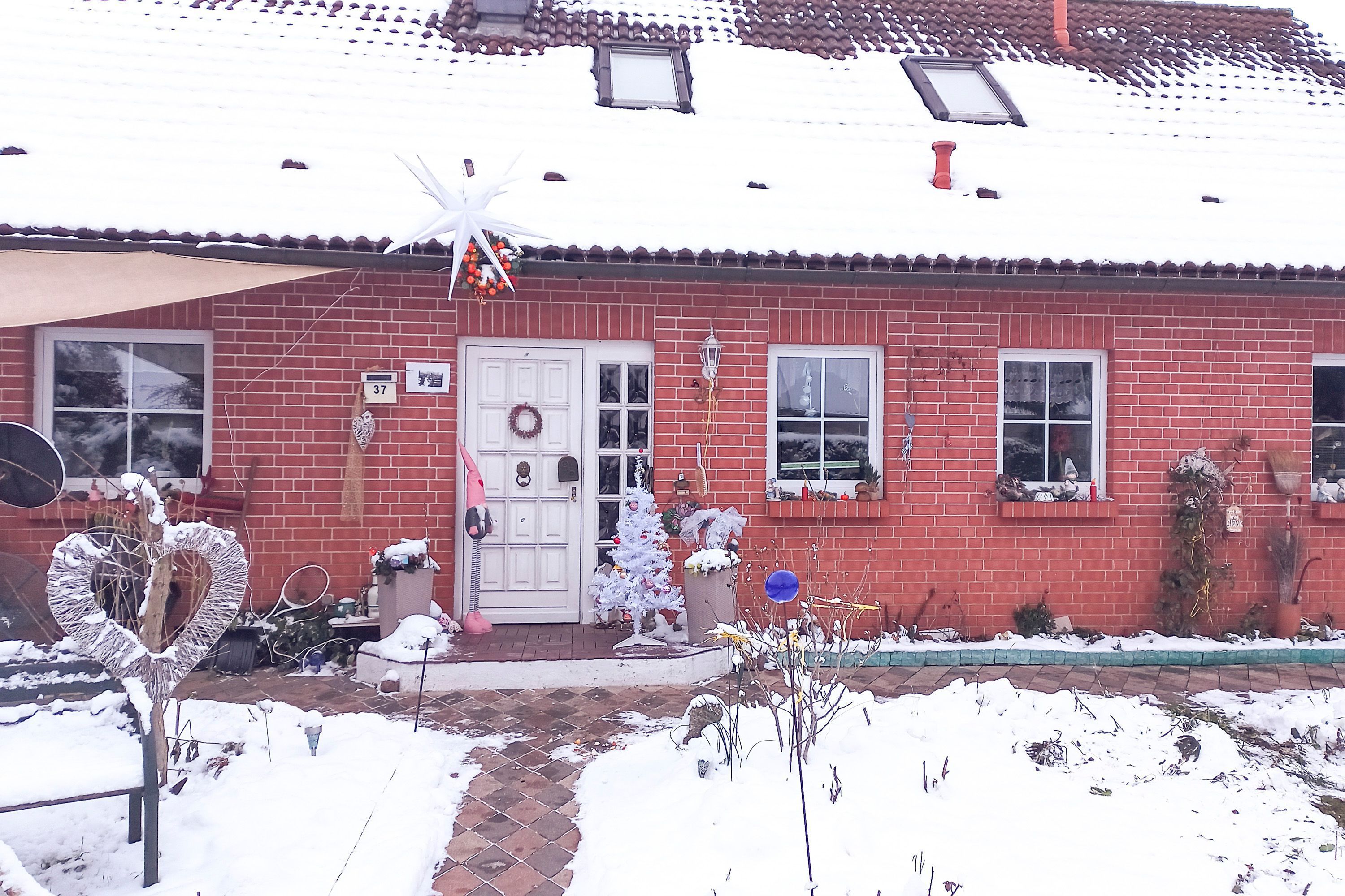 A red brick house with a white door, a wreath, and a Christmas tree.