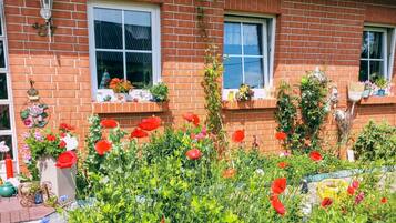 A brick house with two windows, a small porch, and a garden with red flowers.