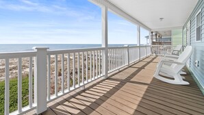 A covered porch with a view of the beach, white rocking chairs, and a dining area. - "Good Times and Tan Lines " - Luxury Oceanfront Home w/ Private Pool, 6 Bedrooms / 5 Bathrooms (Holden Beach)
