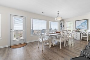 A dining area with a white table and chairs, a chandelier, and a view through the windows.