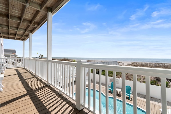 A wooden deck with a pool and chairs, overlooking the ocean.