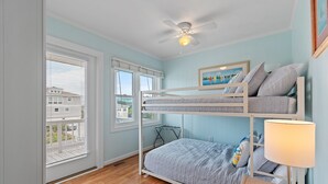 Ein Schlafzimmer mit Etagenbetten, Deckenventilator, Fenster mit Jalousien, einem gerahmten Bild an der Wand und einer Nachttischlampe.