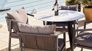 An outdoor patio with a table and chairs, a potted plant, and a window with curtains. - Modern Unit/Beach Walk/Drive to Winery (Port Noarlunga South)