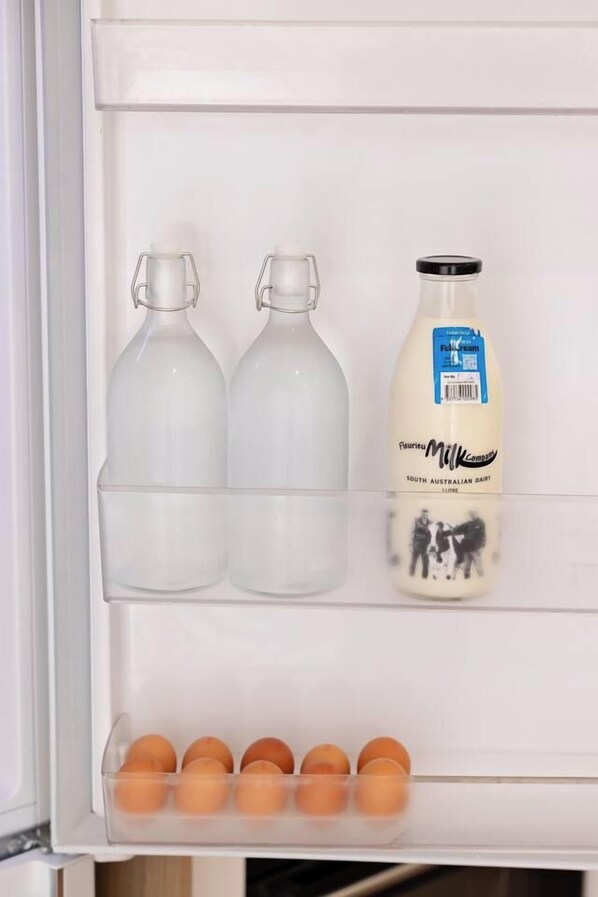 A refrigerator with two clear bottles, a milk bottle, and a carton of eggs.