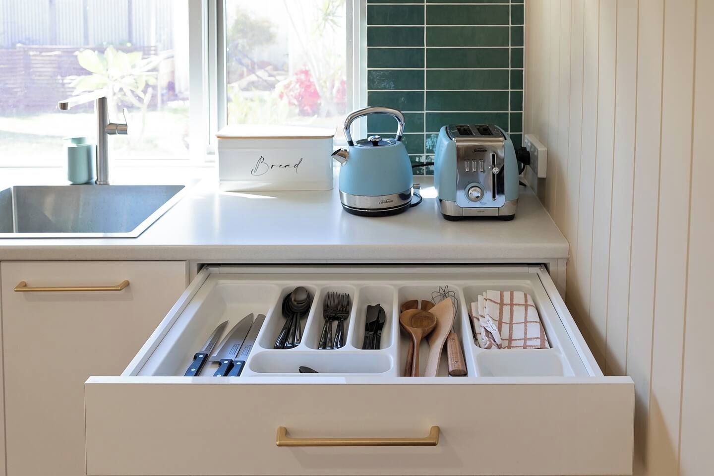 A kitchen with a drawer organizer containing utensils, a kettle, and a toaster on the countertop.