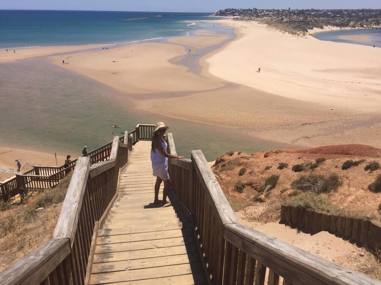 A wooden boardwalk leading to a beach with clear waters and sandy shores.