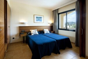 Habitación de hotel con dos camas, cabecera de madera, un cuadro enmarcado en la pared y una ventana con cortinas.