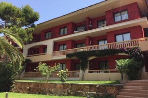 Un hotel de varios pisos con balcones, un muro de piedra y un césped bien cuidado.