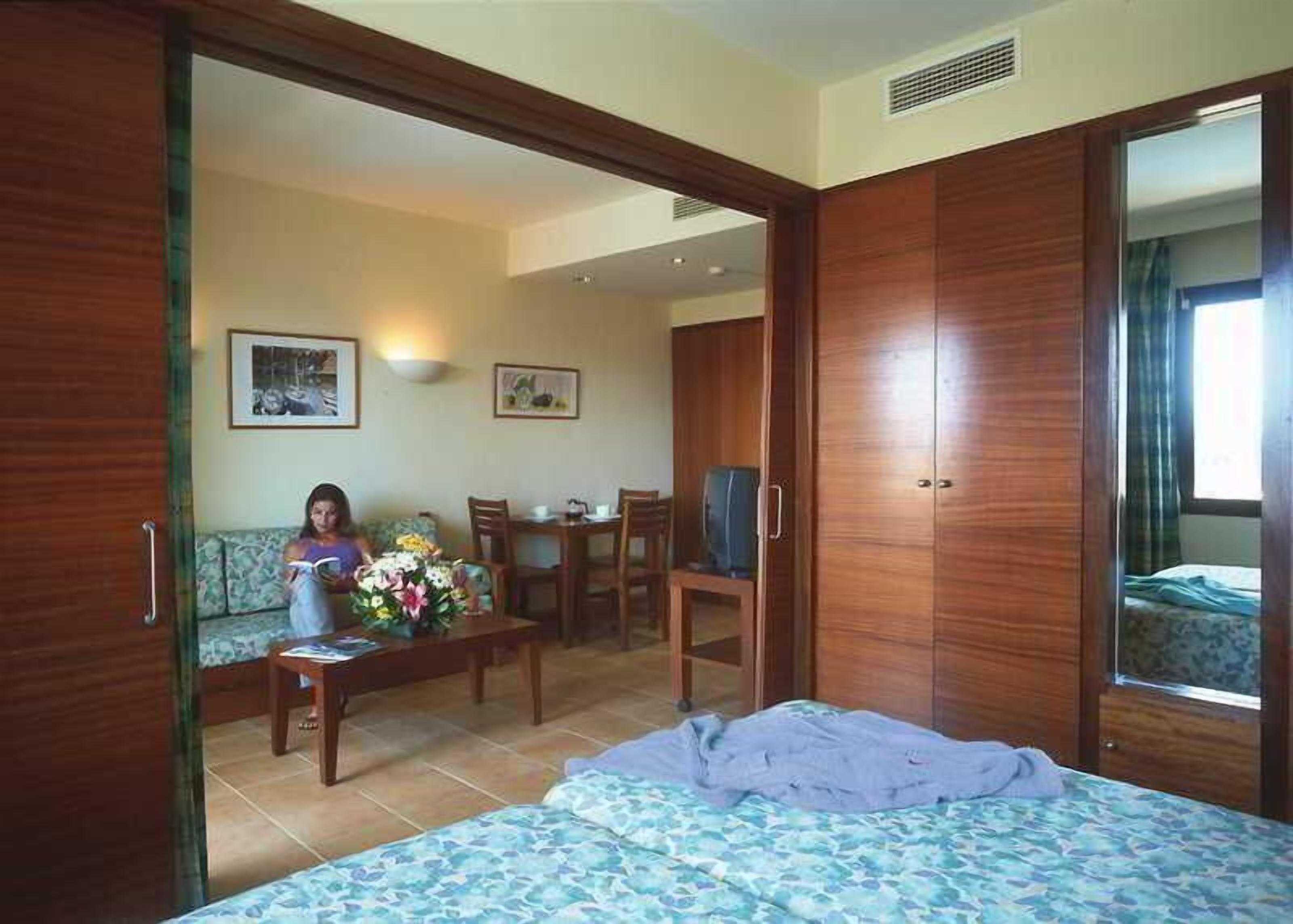 A bedroom with a bed, a desk, a chair, a sofa, and a TV.