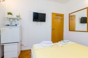 Une chambre d’hôtel comprenant un lit, une télévision, une porte en bois, un miroir, une petite étagère avec des articles de toilette et un réfrigérateur.