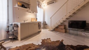 Una cocina moderna con una isla central, una zona de comedor con una silla, una escalera y un televisor de pantalla plana.
