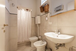 Une salle de bain équipée de toilettes, d’un bidet, d’un lavabo et d’un rideau de douche.