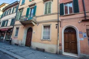 Une rangée de bâtiments aux volets verts, dotés d’un balcon et d’une grande porte en bois.