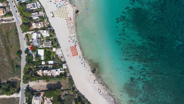 An aerial view of a beach with rows of beach umbrellas and a row of houses adjacent to the shore. - Villa Azzurra (San Vito Lo Capo)