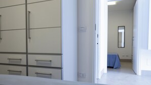A room with a large wardrobe, a bed with a blue cover, and a mirror on the wall. - Villa Azzurra (San Vito Lo Capo)