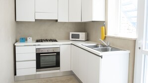 A modern kitchen with white cabinets, a gas stove, an oven, a microwave, and a sink. - Villa Azzurra (San Vito Lo Capo)
