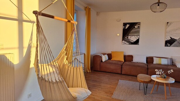 A cozy living room with a hanging chair, a sofa set, a small table, and a rug.